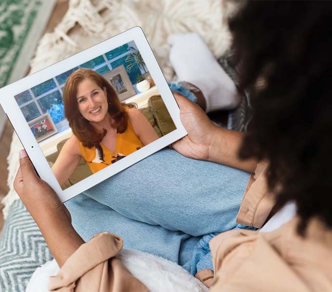 An over-the-shoulder shot of a woman watching a Dressing Well Method Self-Study video on an iPad.